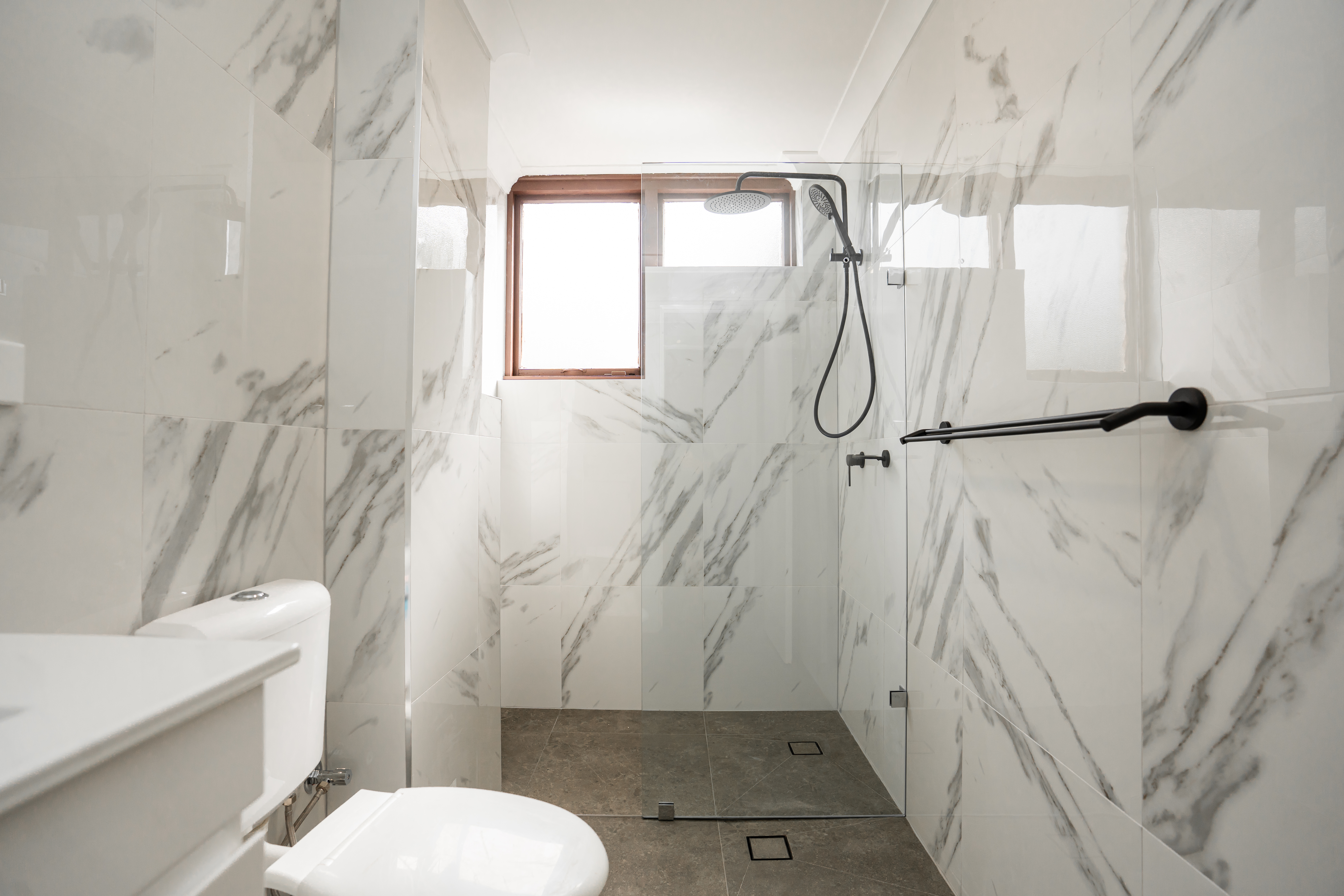 Bathroom renovation — marble wall tiles with black rain shower and glass screen