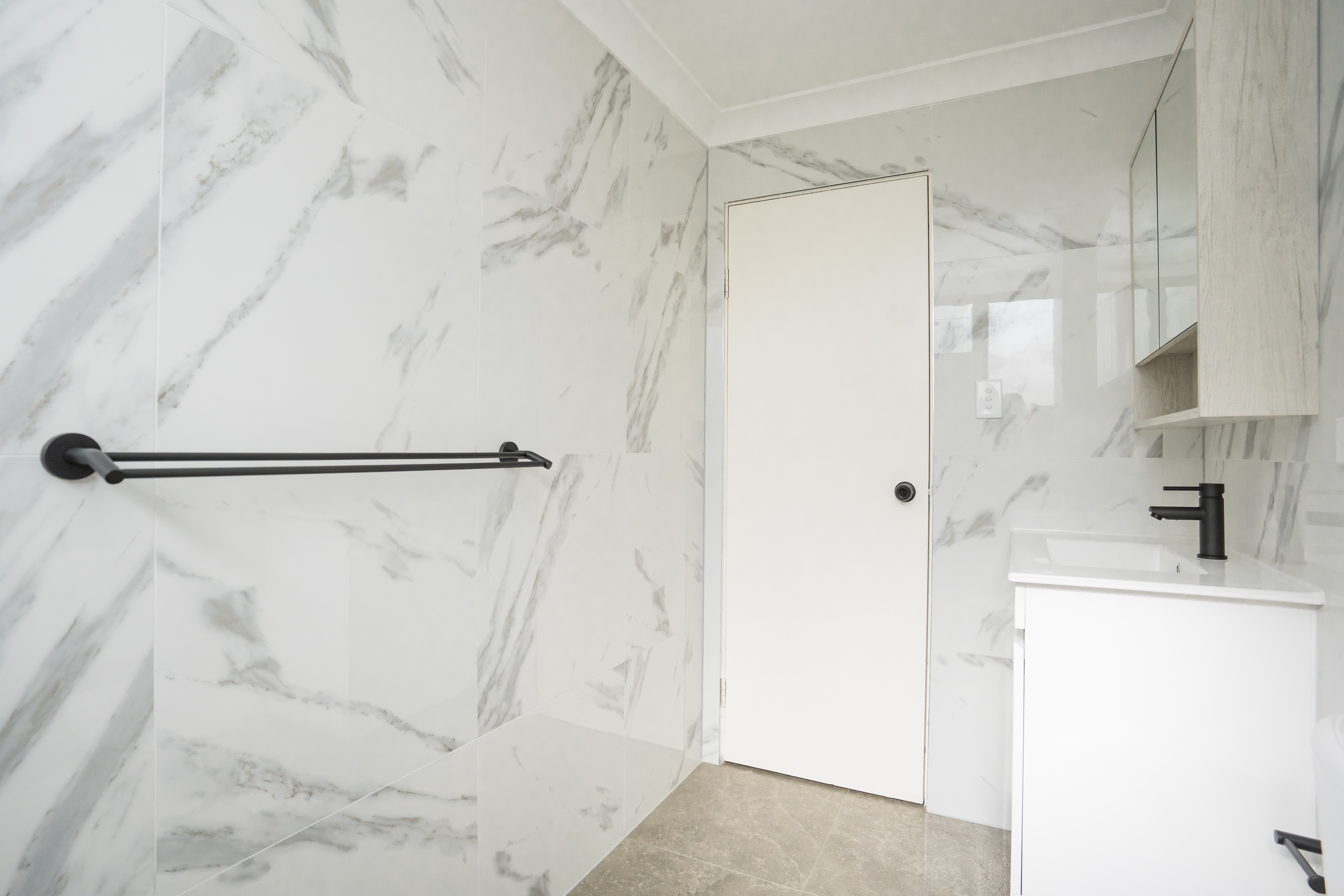 Bathroom wall — marble tiles with black towel rail, door, and vanity