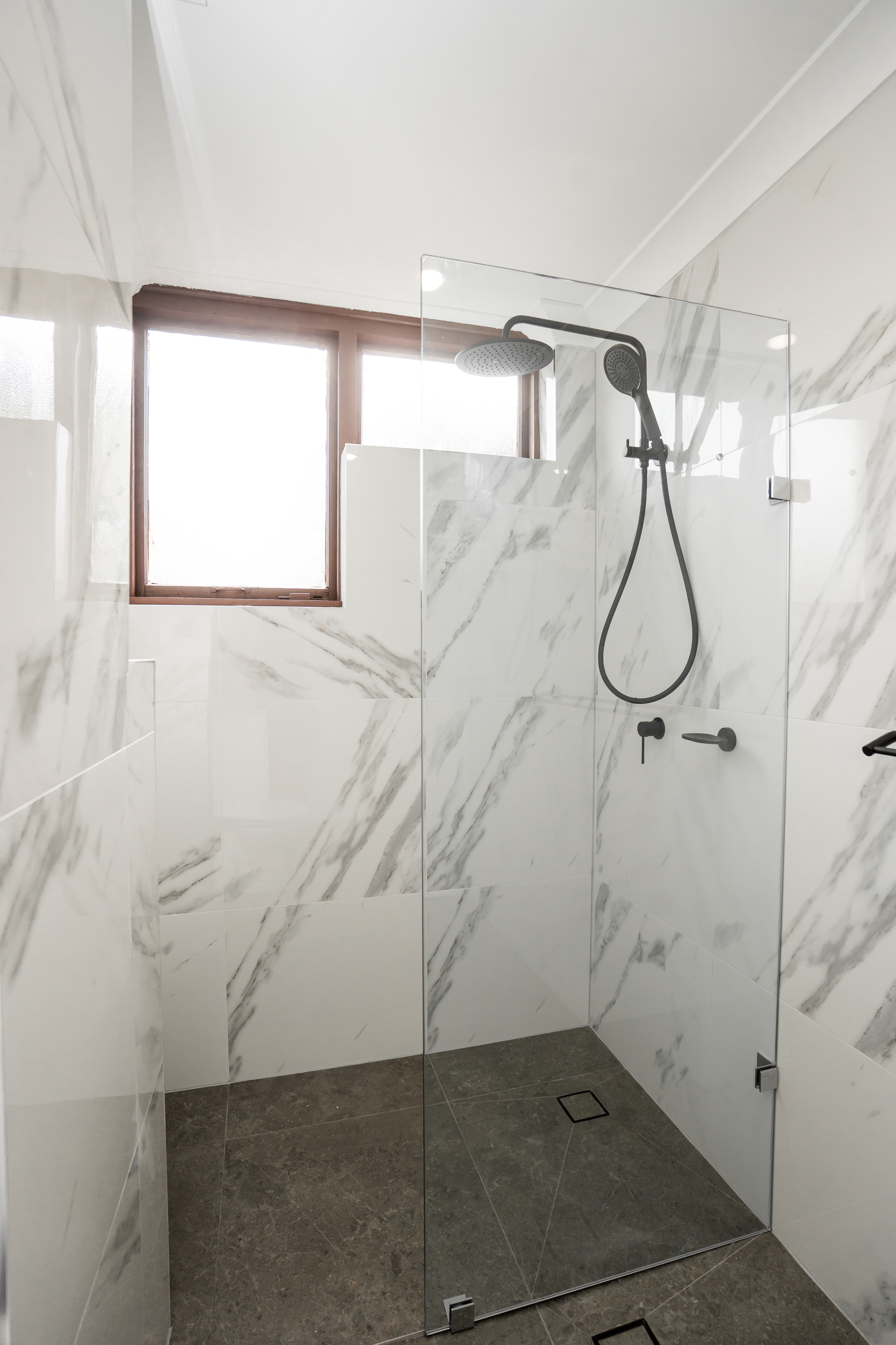 Shower detail — frameless glass screen, marble tiles, black rain showerhead