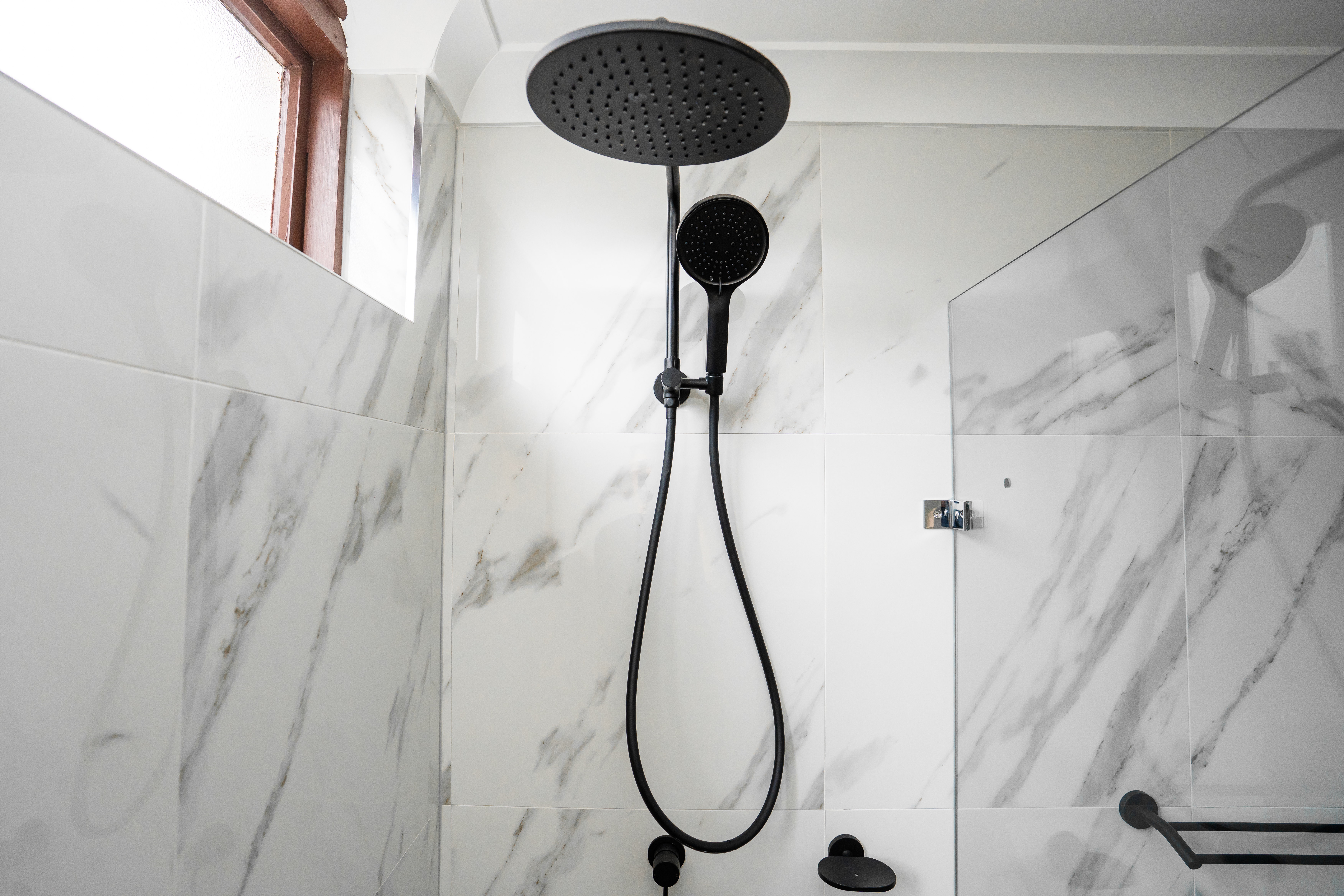 Shower wall — dual showerheads on marble tiles with timber-framed window
