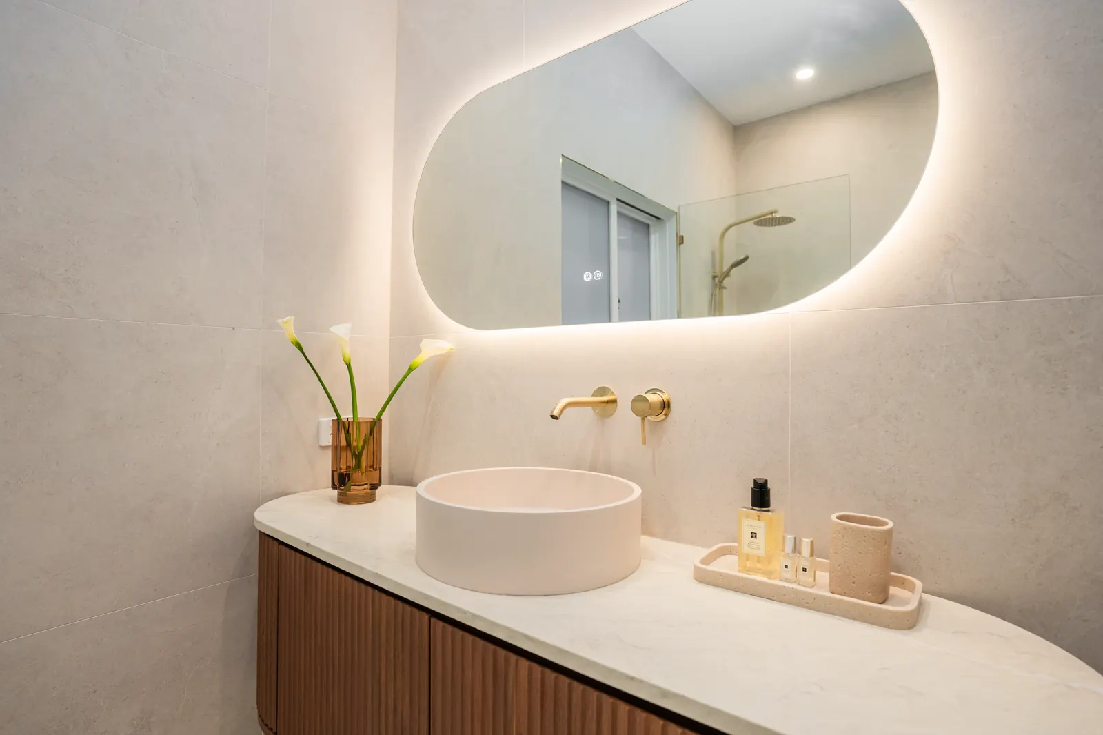 Basin detail — round stone basin with wall-mounted brushed gold mixer on seamless porcelain splashback