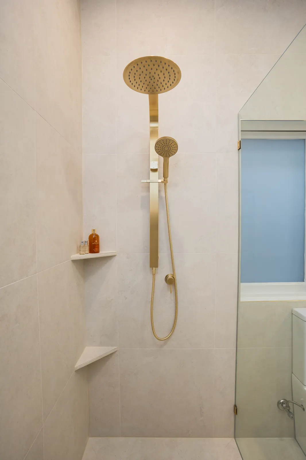 Walk-in shower — brushed gold rain shower set against large-format porcelain wall tiles with tiled corner shelves